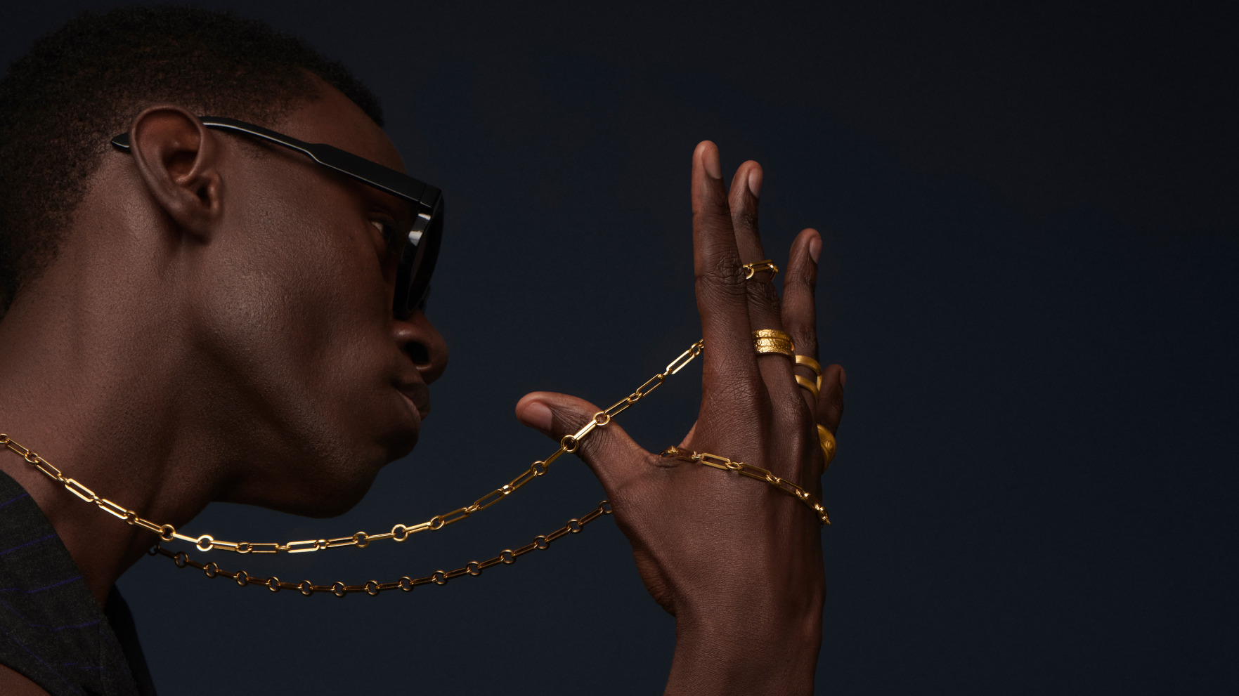 Model in profile wearing gold chain jewelry against a dark background