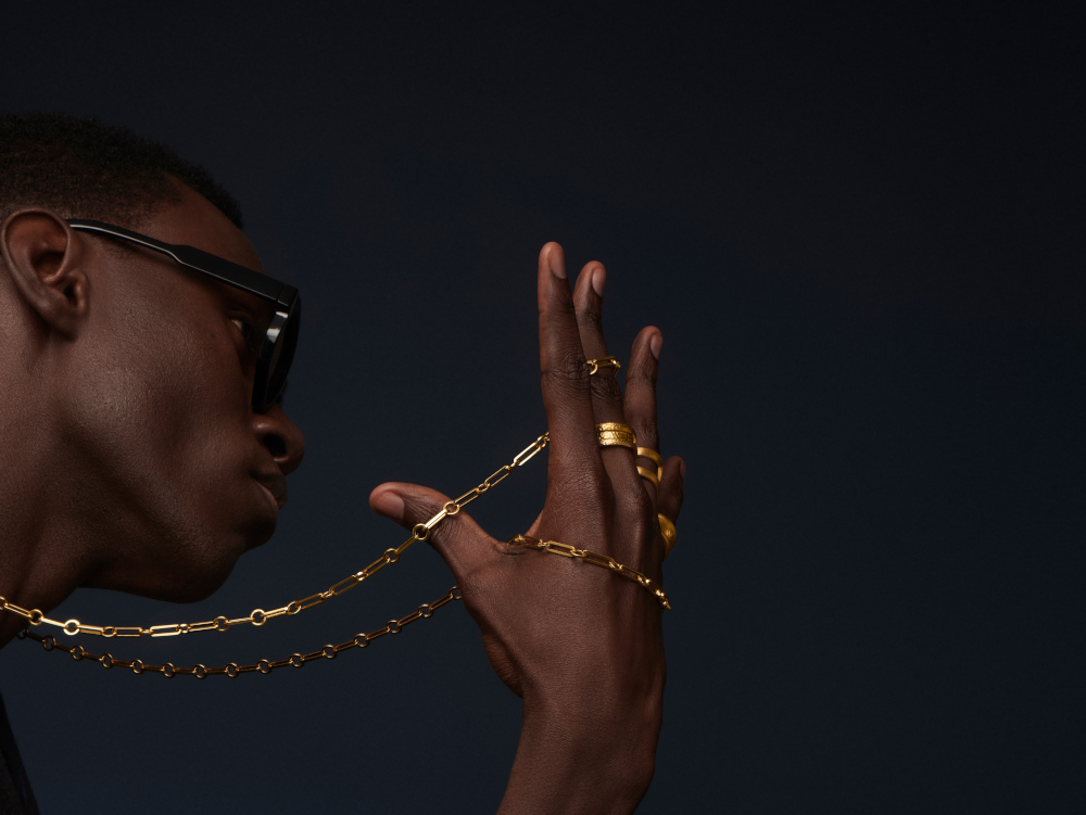 Model in profile wearing gold chain jewelry against a dark background